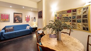 A room with a blue sofa, a wooden dining table with chairs, a quilt on the wall, and framed pictures. - Apartment 'Casa Luna' Opposite Genoa Aquarium (Genova)
