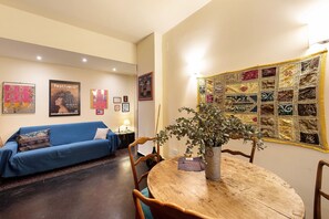 A room with a blue sofa, a wooden dining table with chairs, a quilt on the wall, and framed pictures. - Apartment 'Casa Luna' Opposite Genoa Aquarium (Genova)
