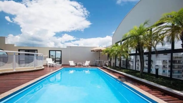 A swimming pool with lounge chairs and palm trees, surrounded by a modern building. - The Palace Moema 501 (São Paulo)