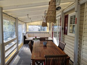 A covered porch with a wooden table and chairs, a cushioned bench, and a wicker hanging light fixture. - Nell's Cabin (Lège-Cap-Ferret)