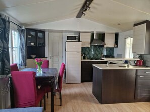 A compact kitchen with a dining area, featuring a table with chairs, a refrigerator, a microwave, and a coffee maker. - Nell's Cabin (Lège-Cap-Ferret)