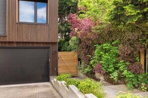 Ein modernes Haus mit einer großen Garagentür, einem Holzzaun und einem Garten mit verschiedenen Pflanzen und einer Kletterpflanze.