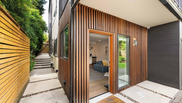 Una casa moderna con fachada de madera, una cocina a la vista y un salón con sofá y mesa de centro.
