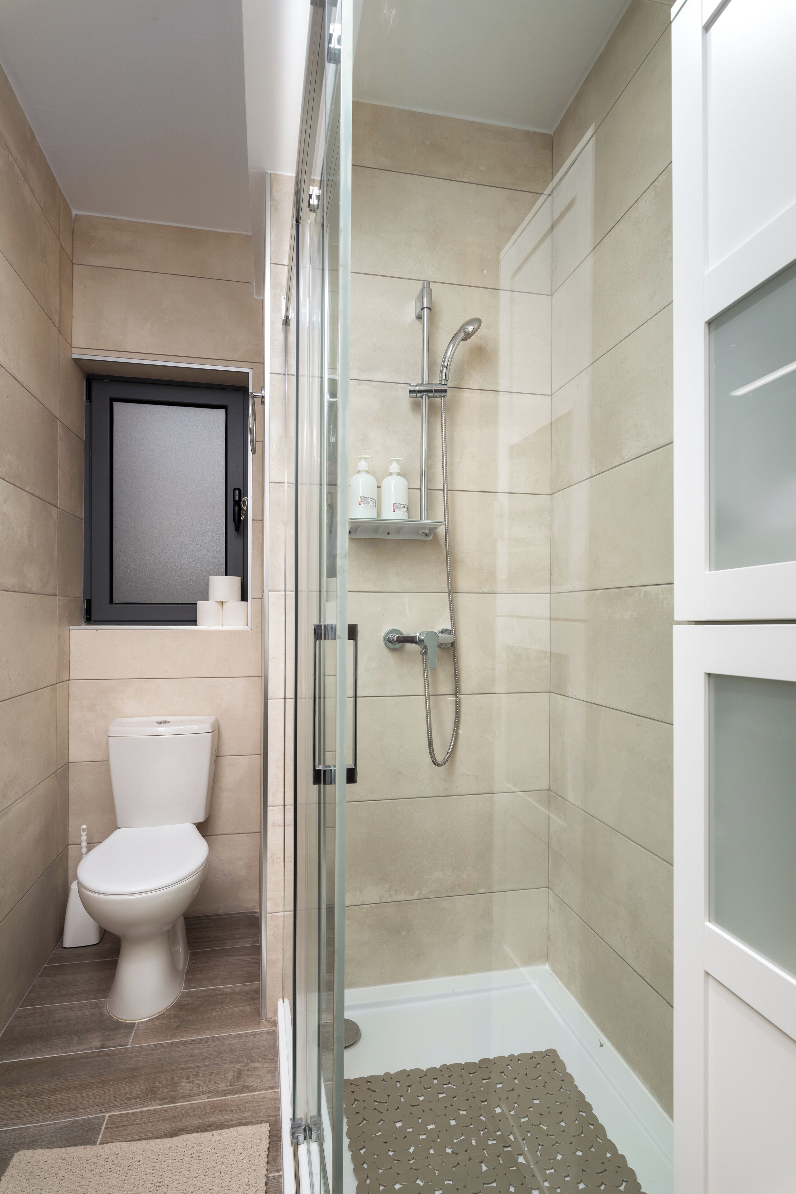 Une salle de bain moderne avec une douche à parois de verre, des toilettes et une étagère contenant des articles de toilette.
