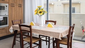A modern kitchen with wooden cabinets, a dining table with chairs, a vase with flowers, and a balcony with a view of buildings. - Chic Stay Near Yacht Marina 2 Balconies (Pietà)