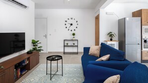 A modern living room with a flat-screen TV, a blue sofa, a small side table, and a wall clock. - Chic Stay Near Yacht Marina 2 Balconies (Pietà)