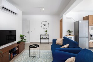 A modern living room with a flat-screen TV, a blue sofa, a small side table, and a wall clock. - Chic Stay Near Yacht Marina 2 Balconies (Pietà)