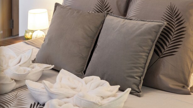 A neatly made bed with a patterned bedspread, two pillows with a leaf design, and a nightstand with a lamp and a decorative item. - Chic Stay Near Yacht Marina 2 Balconies (Pietà)
