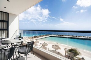 A balcony with a view of a clear blue ocean, a pool, and a table with chairs. - Majestic 2-Bed Ocean Front Suite by Bocobay (Willemstad)