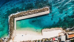 Luftaufnahme eines Strandes mit einem Felsstollen, klarem türkisblauem Wasser und einem Sandstrand.