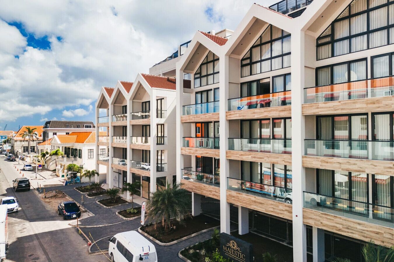 A modern multi-story hotel with balconies, large windows, and a parking area.