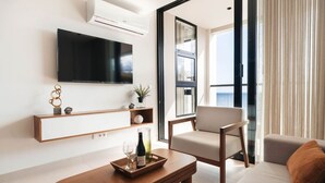 Ein modernes Wohnzimmer mit Flachbildfernseher, einer Couch, einem Sessel, einem Couchtisch und einem Balkon mit Vorhängen.