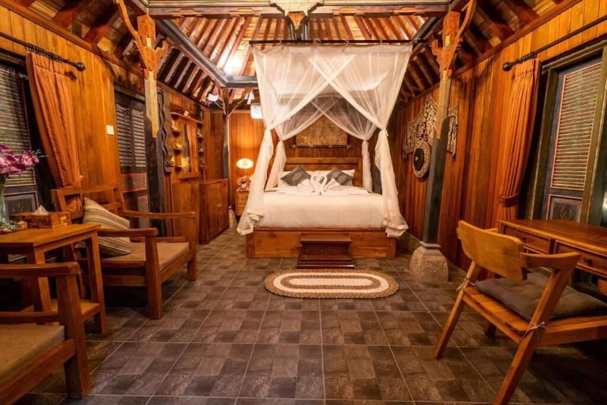 A traditional wooden room with a bed under a canopy, wooden furniture, and a stone statue.