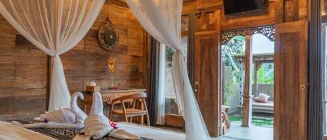 A bedroom with a canopy bed, a small table with chairs, and a view of the outside garden.