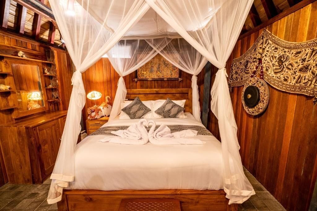 A bed with a canopy, pillows, and towels arranged on it.