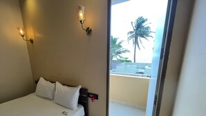 A hotel room with a bed, two wall-mounted lights, and a view of a balcony with palm trees. - The K Inn Wavefront (Tirukalukundram)