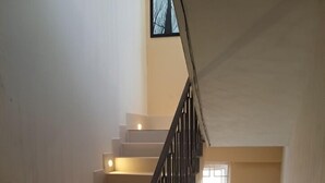 A staircase with a black railing and lights under each step, leading to a landing with a window and a framed picture. - The K Inn Wavefront (Tirukalukundram)