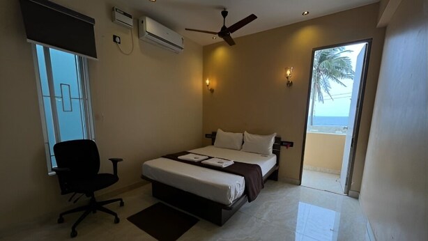 A bedroom with a bed, a desk, a chair, a ceiling fan, and a view of the beach. - The K Inn Wavefront (Tirukalukundram)