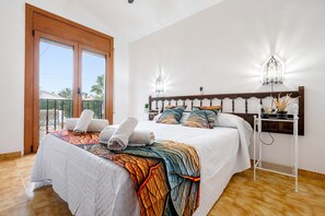 Quarto com uma cama grande, mesa de cabeceira, luminária na parede e vista pela janela.