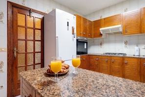 A kitchen with wooden cabinets, a white refrigerator, a stove, and two glasses of orange juice on the counter.