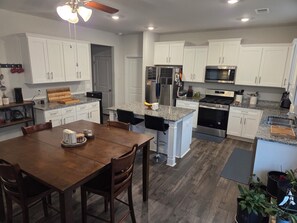 A modern kitchen with white cabinets, granite countertops, stainless steel appliances, and a dining area with a wooden table and chairs. - Luxurious 5-bedroom home in beautiful Graniteville, SC (Graniteville)