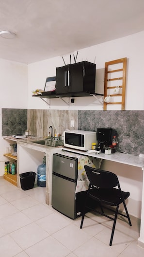 A compact kitchen with a microwave, a small refrigerator, a sink, and a black chair. - Campeche Apartment | Periférico, ING School, QFB, Campus V, Maya Train (San Francisco de Campeche)