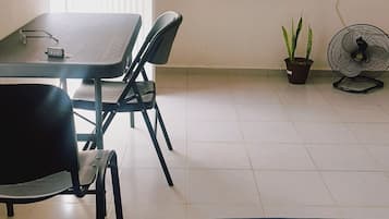 A room with a bed, a table with chairs, a television, a fan, and a potted plant.
