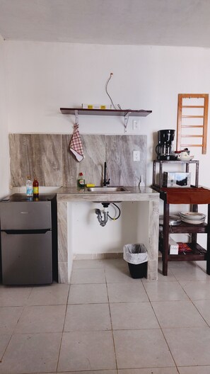 Une petite cuisine équipée d’un réfrigérateur, d’un évier et d’une machine à café posée sur une étagère.
