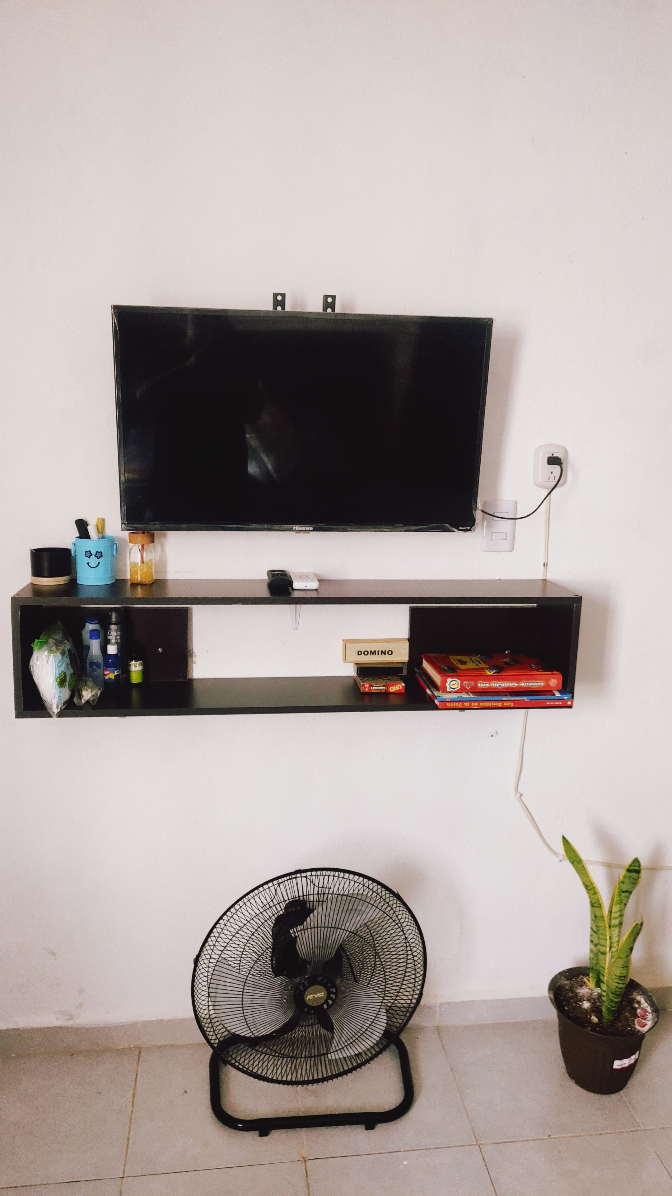 Un televisor montado en la pared con un estante debajo que contiene algunos objetos.
