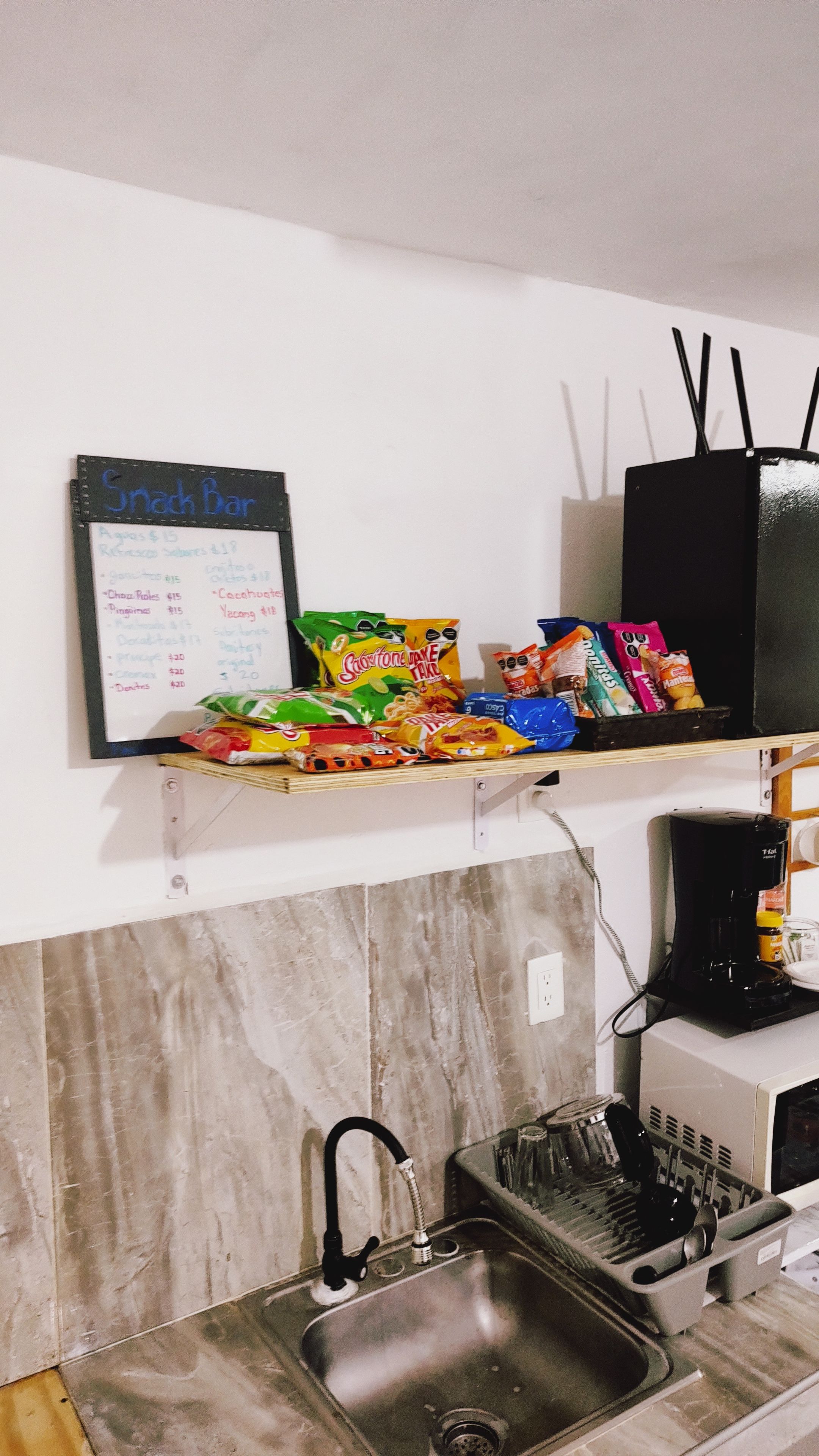 A kitchen with a sink, a coffee maker, and a snack bar sign listing prices.