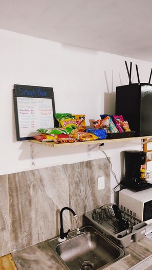 Une cuisine équipée d’un évier, d’une machine à café et d’un panneau indiquant les prix pour les collations.