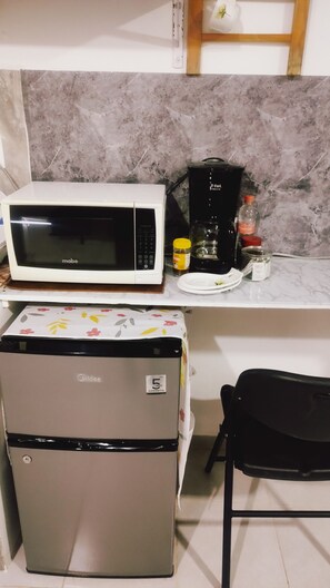 Une cuisine compacte équipée d’un four à micro-ondes, d’une machine à café, d’un réfrigérateur et d’une petite table à manger.