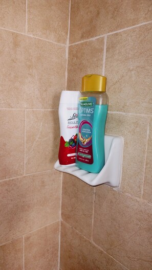 Kylpyhuoneen hyllyllä on pullo Palmolive-shampoota ja pullo Optims-luonnonöljyjä.