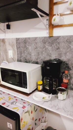 A kitchen with a white microwave, a coffee maker, a jar of honey, a plate, and a jar of jam.
