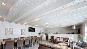 Un grand espace de vie comprenant une table à manger, plusieurs chaises, un canapé et, au fond, un coin cuisine.