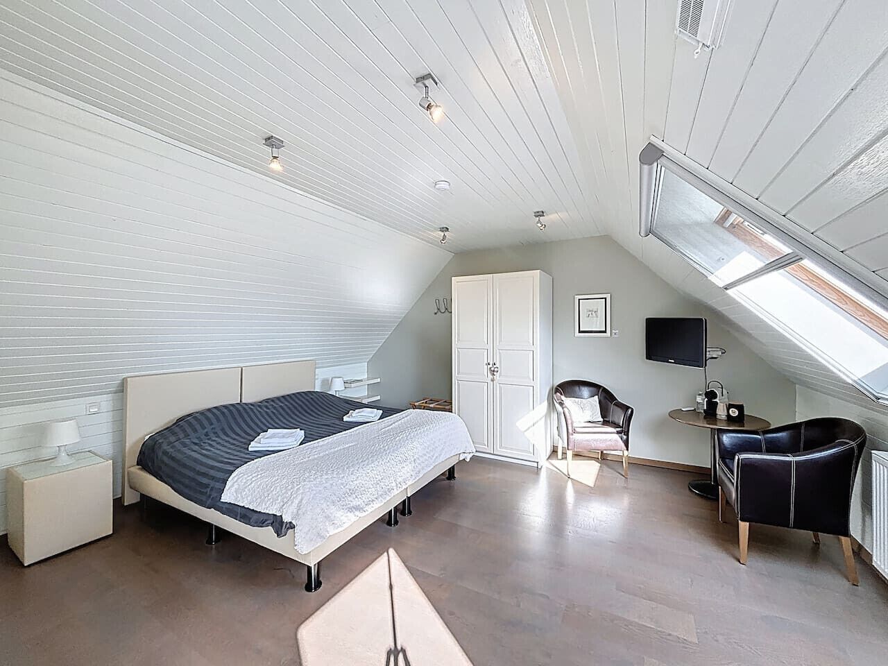 Un dormitorio con cama, mesita de noche, silla, escritorio y televisor.