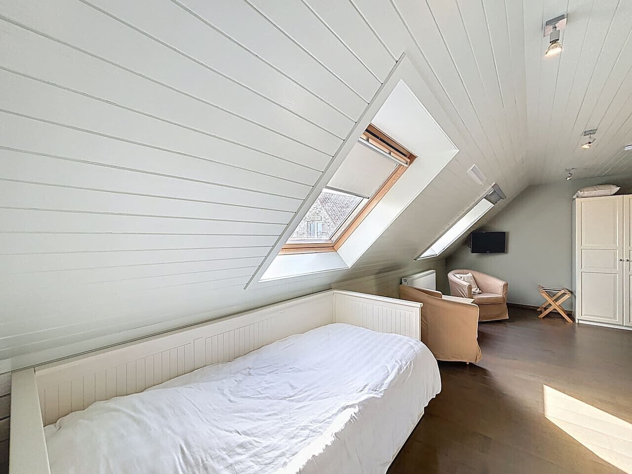 Un dormitorio con tragaluz, una cama, una silla y un televisor.