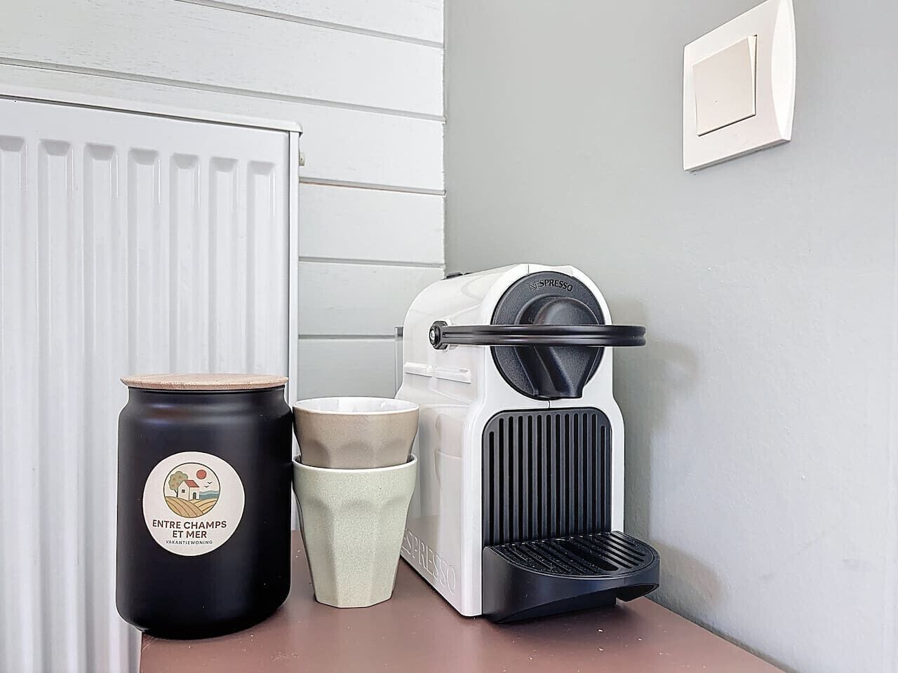 A coffee machine, a ceramic mug, and a black container with a logo on a kitchen counter.