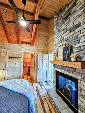 A log cabin interior with a fireplace, wooden walls, and a ceiling fan. - NEW Cabin in Hocking Hills - The Overlook (Logan)