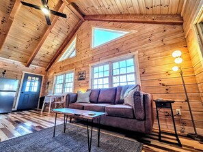 A cozy cabin interior with a wooden interior, a sofa, a table, and a ceiling fan. - NEW Cabin in Hocking Hills - The Overlook (Logan)