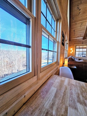 A cabin interior with large windows, wooden walls, and a cozy seating area with a table and chairs. - NEW Cabin in Hocking Hills - The Overlook (Logan)