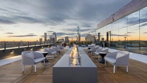 En takterrass med en lång eldstad, sittplatser och utsikt över stadens skyline.