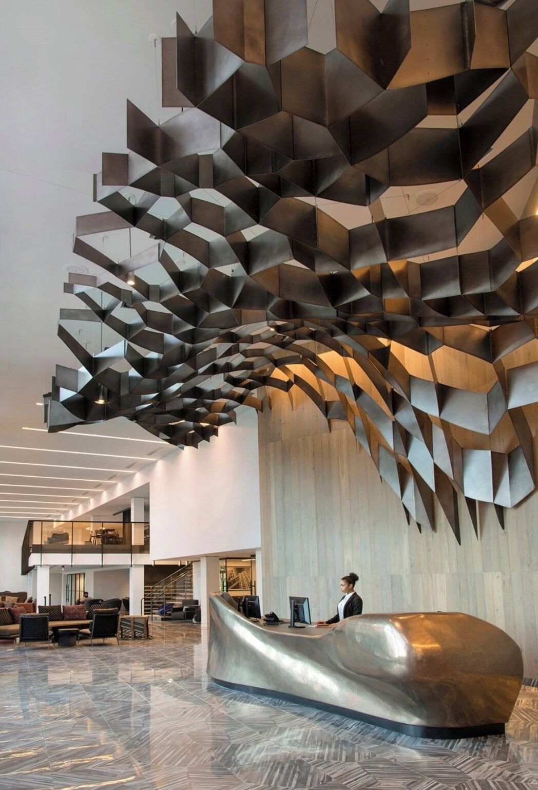 Un vestíbulo moderno con un diseño de pared geométrico único, un mostrador de recepción curvo y un piso de mármol pulido.