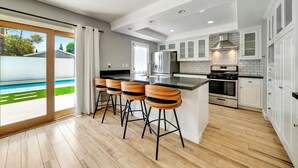 Een moderne keuken met een groot eiland, barstoelen, een koelkast en uitzicht op een achtertuin.