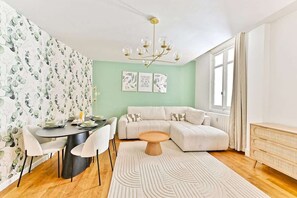 Ein modernes Wohnzimmer mit einer Eckcouch, einem Esstisch mit Stühlen, einem runden Couchtisch und einem gemusterten Teppich.