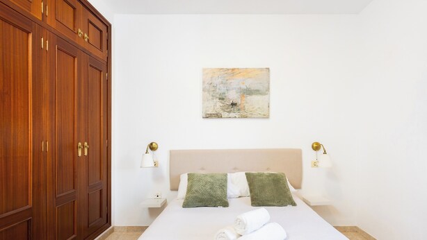 Een hotelkamer met een grote houten garderobe, een bed met witte lakens, twee groene sierkussens en een schilderij aan de muur.