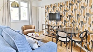 Ett modernt vardagsrum med en soffa, ett matbord med stolar, en tv som är monterad på en vägg med ett mönster och ett fönster med gardiner.