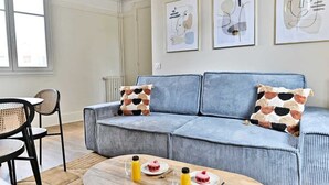 Ett vardagsrum med en blå soffa, två mönstrade kuddar, ett soffbord med drycker och tallrikar samt en matplats med stolar och ett bord.