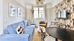 Ett modernt vardagsrum med en blå soffa, ett runt bord och en tv som är monterad på väggen.