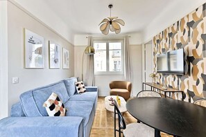 A modern living room with a blue sofa, a round table, and a television mounted on the wall. - Calm and light in the heart of Neuilly (Neuilly-sur-Seine)